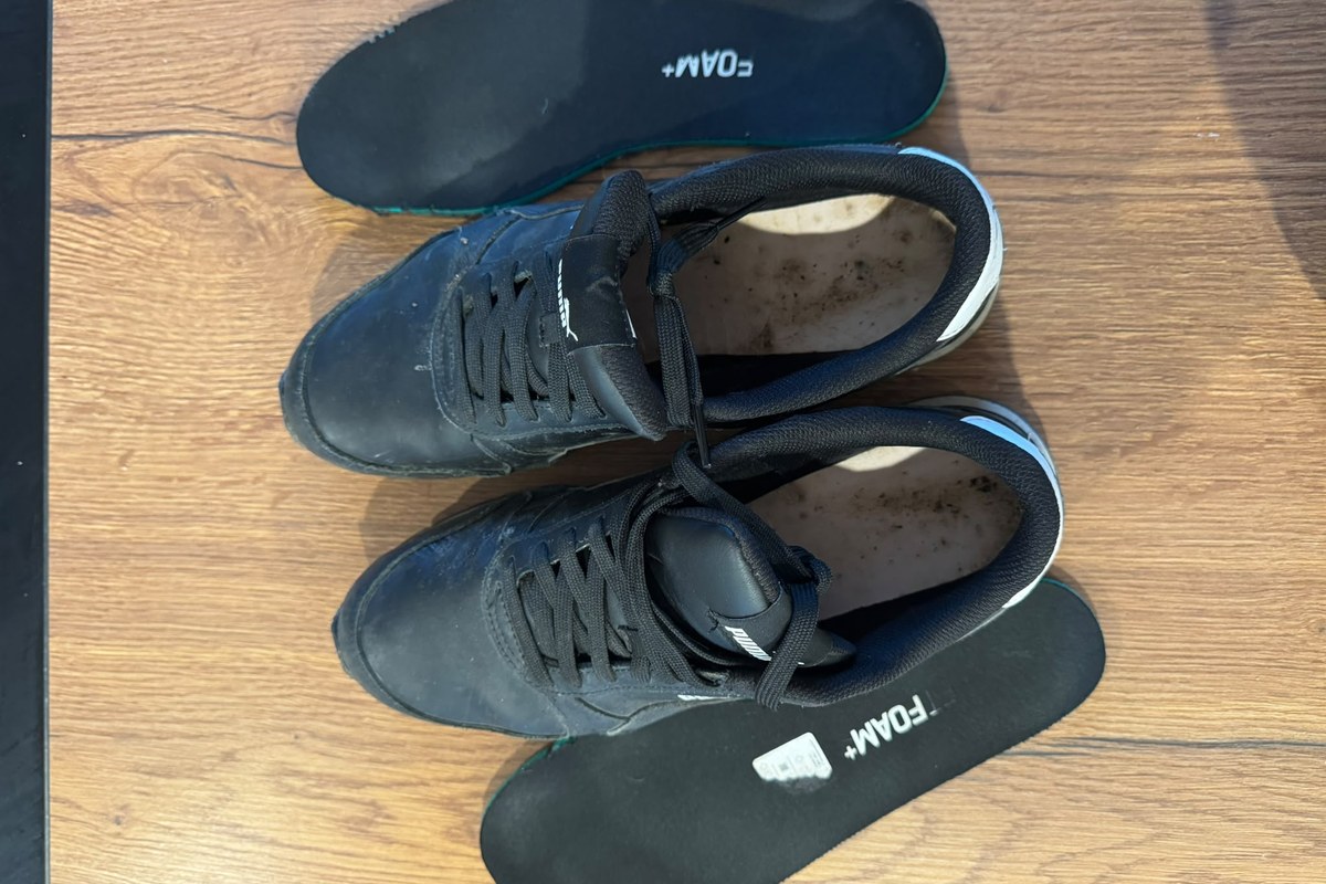 Schwarze Schuhe mit danebenliegenden herausgenommenen Einlegesohlen