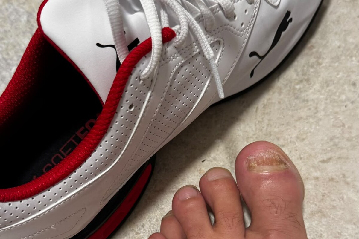 Fuß neben einem weißen Sportschuh auf hellem Boden